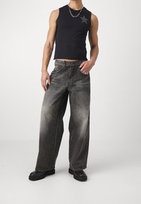 Svart ärmlös topp med stjärndetalj; mörkgrå vida jeans med nitarpå bältet; svarta klumpiga plattformstövlar; slät textur, avslappnad design.