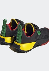 Svarta sportskor har en ventilerande ovandel, en grön gummihäl med texturerade detaljer och en flerfärgad sula i gult och rött.