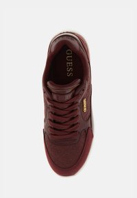 Baskets bordeaux avec motif logo en relief ton sur ton, bout rond et accents dorés. Présentent un système de laçage et une semelle en caoutchouc blanche.