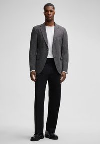 Grau strukturierter Blazer mit Reverskragen, weißem Rundhals-Shirt und schwarzen Hosen. Die Schuhe haben schwarze, klobige Sohlen.