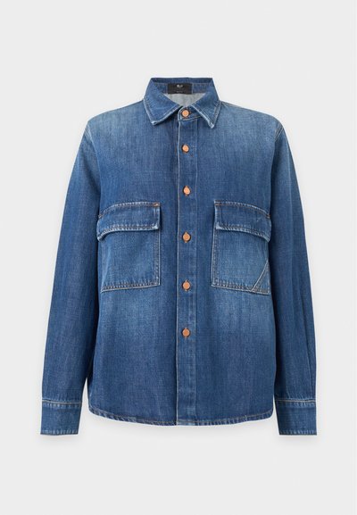Chemise en denim bleu à manches longues avec col, boutons en cuivre sur le devant et deux grandes poches à rabat sur la poitrine.