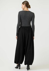 Czarne spodnie z szerokimi nogawkami i marszczonym paskiem w talii, zestawione z dopasowanym szarym topem z długim rękawem. Wykonane z gładkiej tkaniny o subtelnym fakturowaniu.