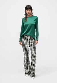 Groen satijnen top met lange mouwen gecombineerd met zwarte en witte broek met een patroon en wijde pijpen. Opvallende geometrische print op de broek en puntige witte schoenen.