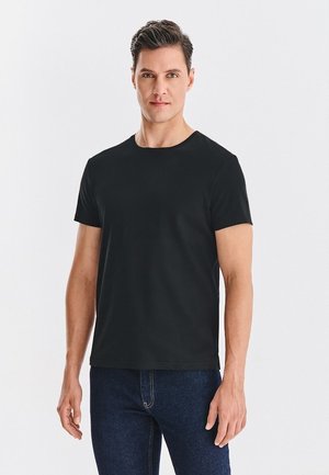 Czarny t-shirt z krótkim rękawem w dopasowanym fasonie z okrągłym dekoltem, uszyty z miękkiego materiału. Noszony z ciemnoniebieskimi dżinsami.