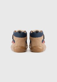 Bruine en marineblauwe peutersneakers met rubberen zolen en klittenbandsluitingen, gezien van achteren op een witte achtergrond.