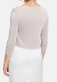 Ljust rosa, metallisk, stickad tröja med trekvartsärmar. Har en rundad halsringning och spetsdetaljer på ärmarna. Slät textur.