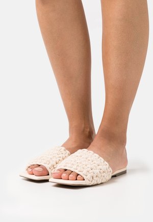 Sandales mules tissées crème avec une large sangle texturée et un bout ouvert. Semelle plate au design minimaliste et couleur neutre.