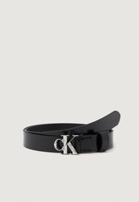 Czarny skórzany pasek z błyszczącym wykończeniem, wyposażony w srebrną metalową klamrę z logo „CK”. Prosty, elegancki design o gładkiej fakturze.