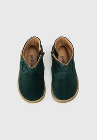 Botas de tobillo de ante verde con una textura suave, que presentan cremalleras laterales y un interior de cuero de un tono beige claro, y suelas de goma beige cosidas.