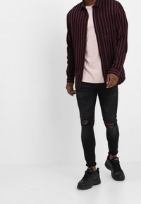 Black and maroon striped long-sleeve shirt over a light pink t-shirt, paired with black ripped jeans and black sneakers.