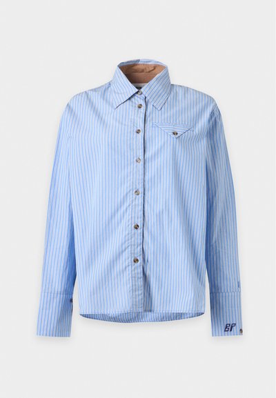 Chemise bleu clair boutonnée avec des rayures verticales blanches, manches longues, col pointu, poche poitrine avec rabat et un petit détail brodé sur le poignet.