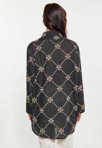 Camicia nera oversize in tessuto leggero, con un motivo geometrico di diamanti e stelle in crema. Con colletto e maniche lunghe.