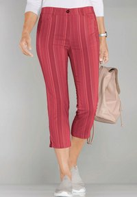 Rote gestreifte Capri-Hosen mit Knopfverschluss und Seitentaschen, im lässigen Schnitt und mit gespaltenem Saum. Tragen mit grauen Sneakern und einem Rucksack.