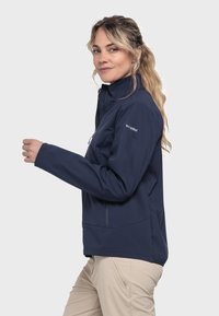 Marinefarbene Softshelljacke mit hohem Kragen, Seitentaschen, Reißverschluss und einer leicht taillierten Passform. Mit Logo auf dem linken Ärmel.