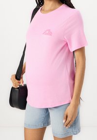 Růžové tričko s krátkými rukávy a květinovým vzorem na hrudi, doplněné světle modrými džínovými šortkami a malou černou crossbody kabelkou.