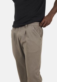 Pantaloni pleated beige realizzati in tessuto leggero con tasche laterali e design a gamba dritta, abbinati a un top nero texture.