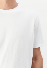 T-shirt en coton blanc avec un col ras du cou, des manches courtes et une texture lisse. Pas de logos ni de motifs visibles. Design simple et classique.