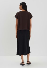 Brauner Crop-Top kombiniert mit einem schwarzen Midirock. Das Outfit hat eine lockere Passform, weiche Stoffe und ein einfaches Design ohne Muster.