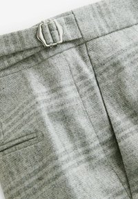 Sive vune hlače s teksturiranim uzorkom, koje imaju srebrnu metalnu kopču i detalje sa bočnim džepovima.