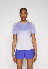 Μωβ αθλητική μπλούζα με κοντά μανίκια, με πιο ανοιχτόχρωμες πάνελ στους ώμους και υφή με σχέδιο. Συνδυάζεται με μπλε σορτς, κατασκευασμένα από ελαφρύ υλικό.