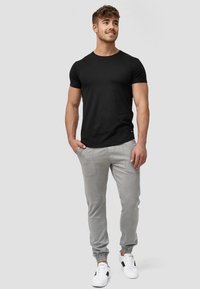 Camiseta negra de manga corta combinada con pantalones ajustados grises claros que cuentan con bolsillos, puños acanalados y zapatillas blancas con detalles en negro.
