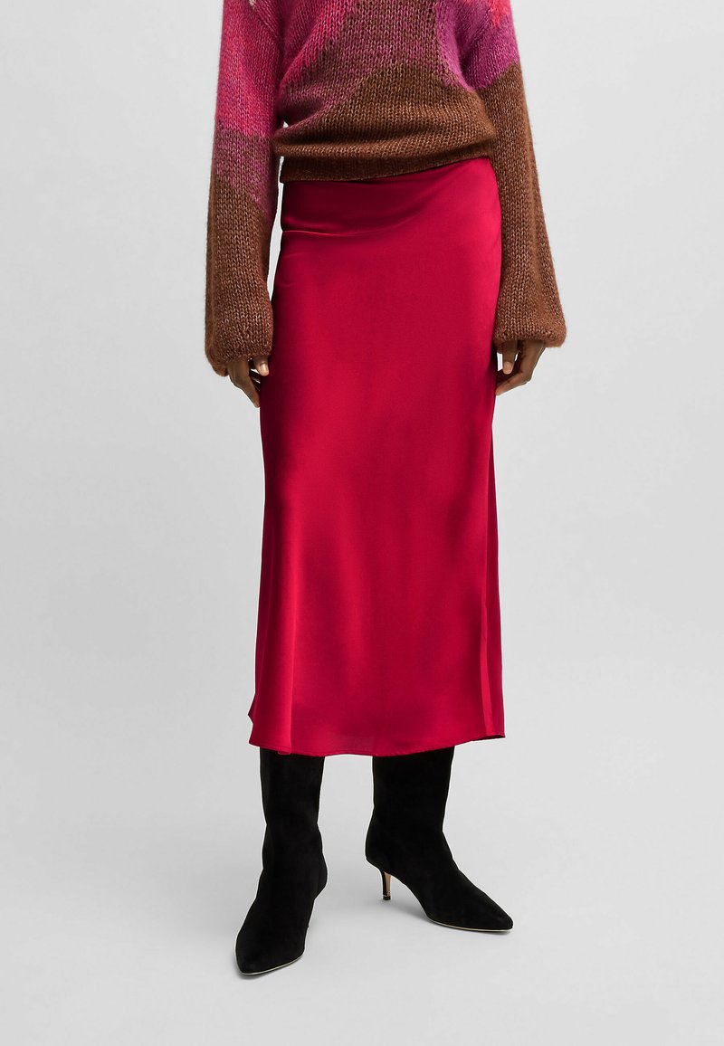 Red satin midi skirt with a smooth texture, featuring a high waist and a straight silhouette. Styled with a brown knit sweater and black boots.