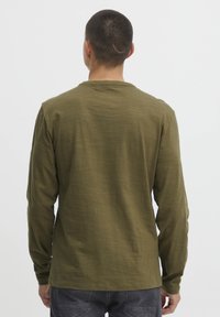 Hosszú ujjas, olíva zöld ing, puha anyagból, kerek nyakkal és laza szabással. Minimalista design, látható minták nélkül.