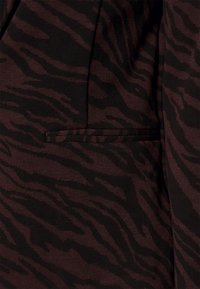 Brun och svart tiger randigt tyg med slät textur; har en smal, vinklad ficka på vänster sida.