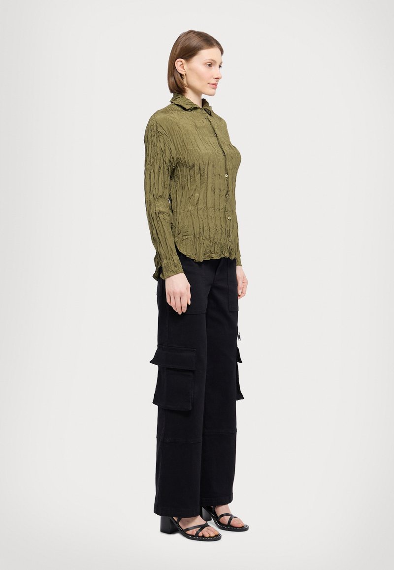Olive green crinkled button-up shirt paired with black cargo pants featuring multiple pockets. Model wears black heeled sandals.