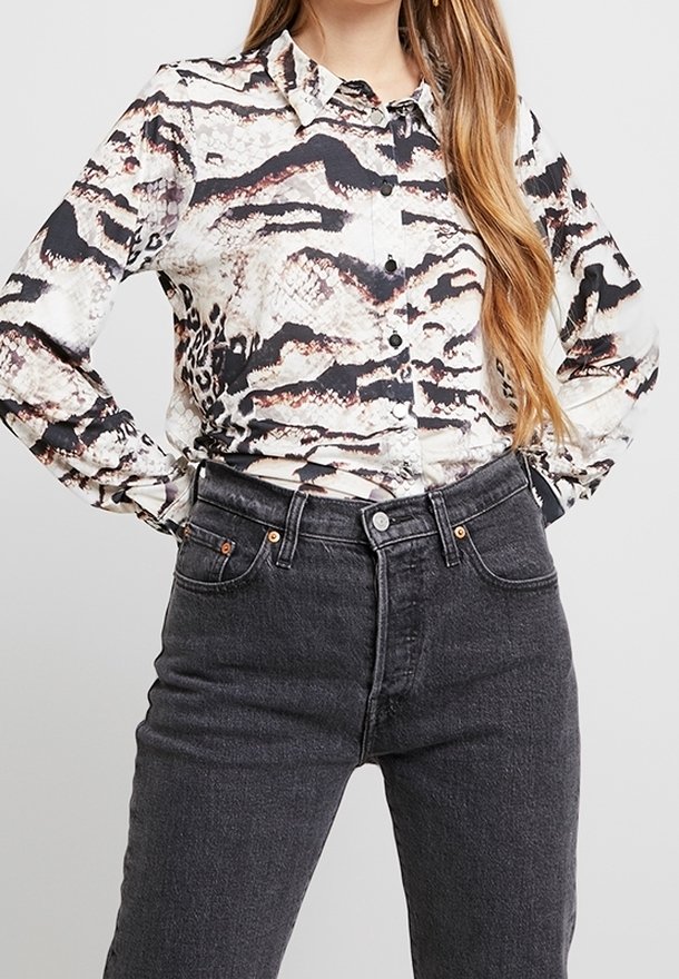Camicia a maniche lunghe con bottoni e motivo a stampa serpente in beige, nero e grigio; abbinata a jeans neri in denim a vita alta.