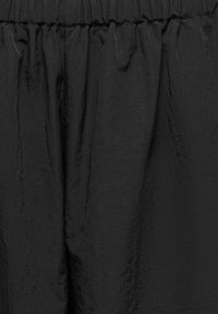 Rideau en tissu noir avec un sommet plissé et une texture subtile, suspendu droit avec de doux plis verticaux.