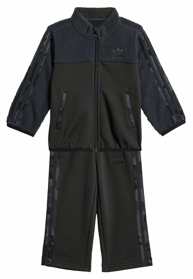 Černý teplákový komplet vyrobený z fleecu a polyesteru. Sestává z bundy na zip s vzorovanými rukávy a kalhot elastickým pasem. Ozdobený logem.