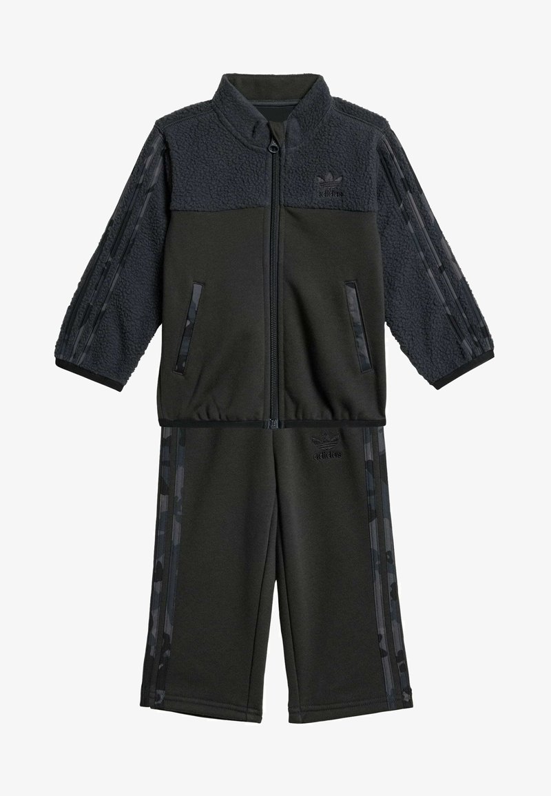 Černý teplákový komplet vyrobený z fleecu a polyesteru. Sestává z bundy na zip s vzorovanými rukávy a kalhot elastickým pasem. Ozdobený logem.