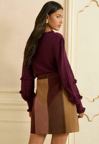 Aansluitende bordeauxrode trui met gestructureerde, volants mouwen, gecombineerd met een meerlagige suède rok in bruin- en bordeauxtinten.