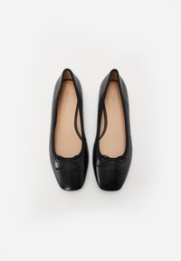 Bailarinas de cuero negro con punta redonda, detalles sutiles de lazo en la parte delantera y una textura suave. El interior es beige.