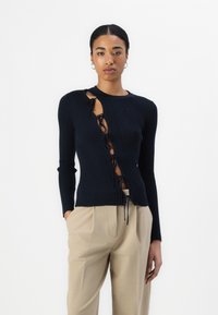 Top de manga larga de canalé en color navy con corte lateral y detalle de cordones. Combinado con pantalones beige ajustados.