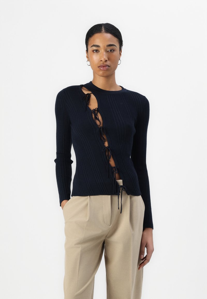 Top de manga larga de canalé en color navy con corte lateral y detalle de cordones. Combinado con pantalones beige ajustados.
