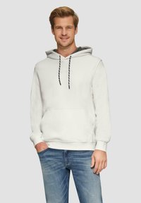 Haut à capuche blanc avec une poche avant, une capuche réglable et des cordons noir contrastants. Associé à un jean bleu pour un look décontracté.