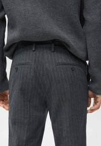 Maglione a coste grigio scuro abbinato a pantaloni scuri a righe, che mostrano una vestibilità su misura e due tasche posteriori con bottoni.