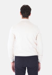 Maglione di un leggero colore crema con colletto e polsini a costine, realizzato in un morbido materiale knit, abbinato a pantaloni blu scuro, visto da dietro.