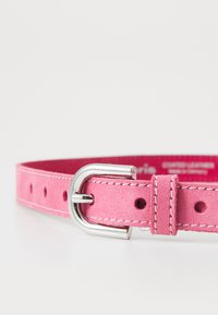 Rosa semsket belte med en sølvmetallspenne, med stikkingdetaljer og flere hull for justering. Myk tekstur og glatt overflate.