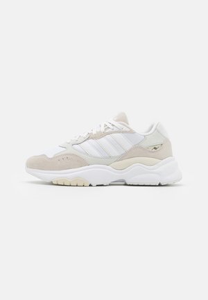 Weißer und beiger Sportschuh mit klobiger Sohle, Veloursleder-Overlays, drei Seitenstreifen und Schnürverschluss auf einfarbigem Hintergrund.