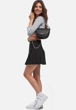 Borsa a tracolla nera trapuntata con forma arrotondata e accessori dorati. Abbinata a una gonna plissettata nera e sneakers bianche, con maniche lunghe a righe.