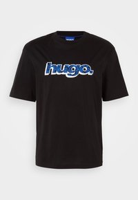 Musta puuvillainen t-paita, jossa on lyhyet hihat ja suuri valkoinen ja sininen "hugo."-logo kukkakuviolla. Pyöreä pääntie.
