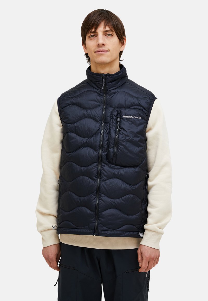 Vest puffer de culoare bleumarin cu un design matlasat, guler înalt, fermoar complet și buzunar frontal. Purtați peste un hanorac de culoare deschisă.