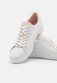 Baskets blanches en cuir avec cols et languettes rembourrés rose pâle, lacets blancs et petit logo MKL argenté sur le lacet avant.