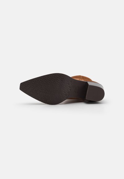 Chaussure à talon haut en suède marron avec un bout pointu et une semelle en caoutchouc noir texturé. La semelle présente un motif de traction pour une meilleure adhérence.