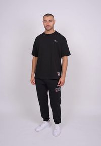 Zwarte katoenen T-shirt met korte mouwen en een klein logo, gecombineerd met donkere sweatpants met opgestikte zakken en witte sneakers.