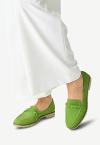 Groene leren loafers met gevlochten accent, platte rubberen zool en ronde neus, gecombineerd met witte wijde broek.