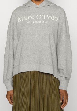 Personne portant un sweat à capuche gris avec le texte « Marc O’Polo Est. in Stockholm » et une jupe plissée vert olive.